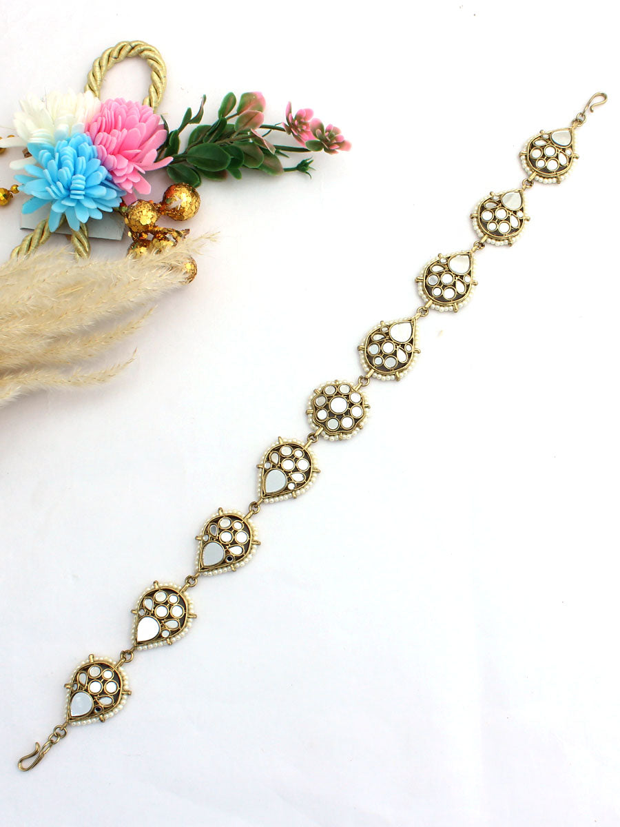 Golden Sheeshphool with intricate circular designs on a white surface, surrounded by dried and fresh flowers.